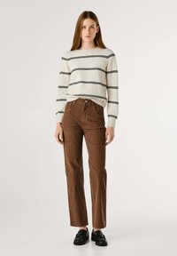 Gestreepte crèmekleurige en zwarte gebreide trui, hooglopende bruine corduroybroek en zwarte loafers. Casual outfit met verschillende texturen en kleuren.