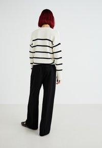 Sweter w paski w kolorze kremowym z czarnymi paskami, dopasowany do luźnych czarnych spodni. Do charakterystycznych detali należą ściśnięte mankiety oraz płaskie buty z ćwiekami.