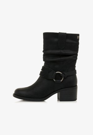 Bottine noire avec un dessus décontracté, décorée d'une sangle texturée et d'un accessoire circulaire, dotée d'un talon empilé. Matériau synthétique lisse.