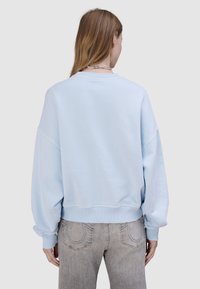 Jasnoniebieska krótka bluza z opuszczonymi ramionami, ściągaczami na mankietach i dole; zestawiona z szarymi jeansami z detalem przeszycia na tylnej kieszeni.