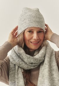 Berretto lavorato a maglia grigio chiaro con una leggera punta sulla sommità, abbinato a una sciarpa morbida e strutturata dello stesso colore avvolta intorno al collo.