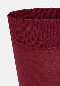 Rote Stricksocke mit einem strukturierten, gerippten Bund und glattem Schaft. Der Stoff ist weich und dehnbar, geeignet für angenehmes Tragen.