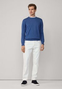 Niebieski sweter dzianinowy z okrągłym dekoltem, zestawiony z białymi dżinsami o prostych nogawkach i czarnymi butami sportowymi na sznurowadłach. Czysty, minimalistyczny design stroju.