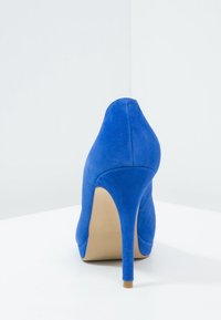 Modrá semišová vysoká podpatek s špičatou špičkou a tenkým stiletto podpatkem; hladká textura a jednoduchý design, minimální akcenty, světlá hnědá podrážka.