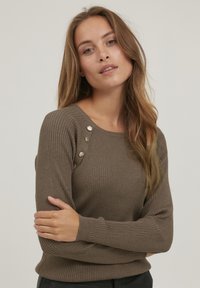 Brauner gerippter Pullover mit Bootsausschnitt, der dekorative Knöpfe an der Schulter und enganliegende lange Ärmel aufweist. Weiche Textur und lässiges Design.