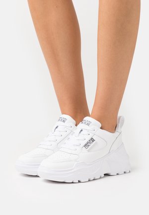 Baskets blanches à semelle épaisse, tige en cuir lisse, détails perforés, design à lacets et logo sur la languette.