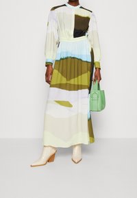 Pitkä, monivärinen mekko, jossa on abstrakteja kuvioita vihreän, sinisen ja beigen sävyissä, puffihihat ja vyötäröltä kiristetty. Yhdistetty vaaleisiin saappaisiin ja vihreään käsilaukkuun.