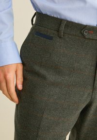 Pantalons en laine à carreaux gris avec une finition texturée, dotés d'une poche accent bleu et d'une fermeture à bouton. Une coupe ajustée est évidente.