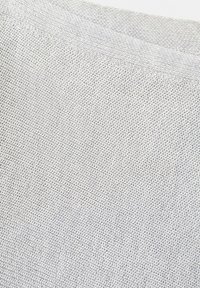 Gros plan sur un tissu tricoté gris clair montrant une texture détaillée de petits points de boucle sur une surface textile douce.