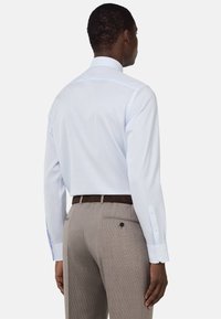 Camicia azzurra a maniche lunghe con colletto a bottoni, abbinata a pantaloni grigi chiari texture e una cintura marrone.