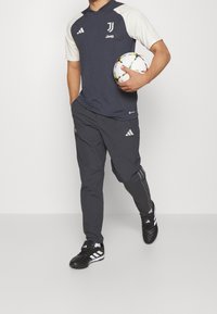 Camiseta deportiva de la marina con acentos blancos, marcada con "Juventus" y "Jeep," combinada con pantalones gris oscuro. Zapatillas deportivas negras con rayas blancas.