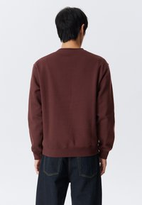 Brauner Sweatshirt mit gerippten Bündchen und Saum, ausgestattet mit einem Rundhalsausschnitt. Der Stoff wirkt weich mit einer strukturierten Oberfläche.