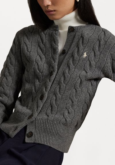 Grijze kabelgebreide cardigan met knoopsluiting, geribde manchetten en rand. Kleine logo-accent op de borst. Zacht, textuurwol stof.
