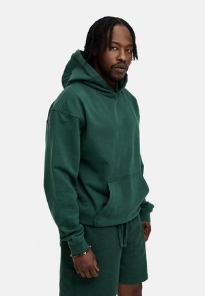 Hooded sweatshirt in dark green fleece, featuring a front kangaroo pocket and ribbed cuffs, paired with matching shorts.