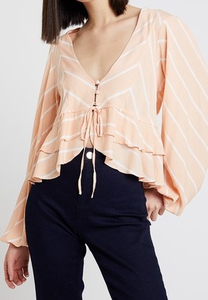 Bluzka w paski brzoskwiniowo-białe z długim rękawem, dekoltem w serek, wiązaniem z przodu i falbaną na dole, zestawiona z czarnymi spodniami z wysokim stanem.