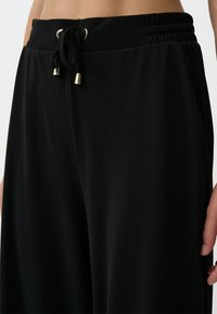 Zwarte drawstringbroeken van zachte stof, met een elastische tailleband, een slank ontwerp en goudkleurige metalen accenten op de koorden.