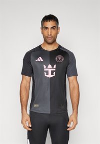 Svart och mörkgrå fotbollsdräkt med korta ärmar, prydd med en rosa logotyp och kronedesign. Tillverkad av lättviktig tyg.