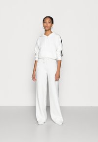 White hoodie with drawstring and side stripes, paired with matching wide-leg pants. Soft fabric with a textured finish. Minimalist design.