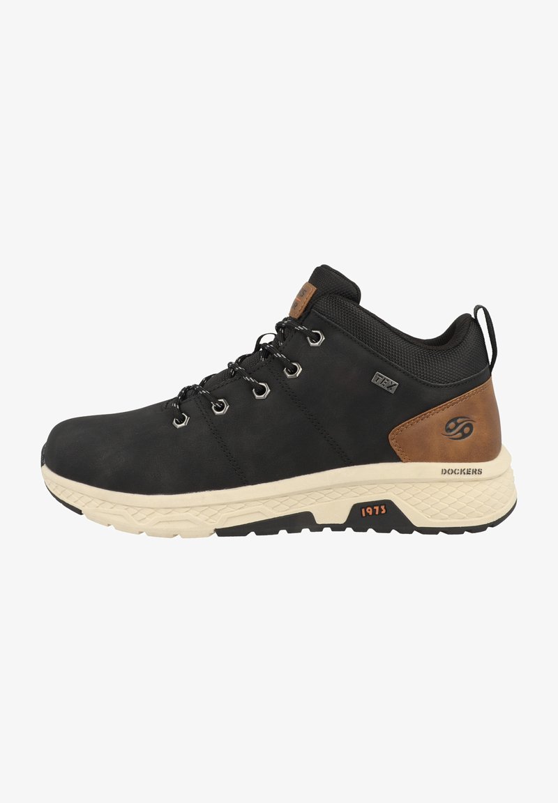 Scarpa da trekking nera con tomaia sintetica, dettagli testurizzati, intersuola crema e suola in gomma. Presenta occhielli in metallo e un'etichetta con logo sul tallone.