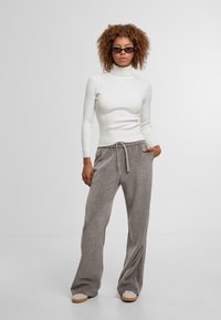 Witte gestreepte coltrui en grijze wijde corduroy broeken met een trekkoord. Model draagt donkere zonnebril, handen in de zakken.