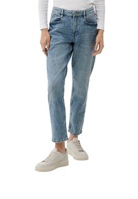 Světle modré denimové džíny s vysokým pasem a tapered nohavicemi. Obsahují přední kapsy a zapínání na zip/knoflík. Kombinováno se světlejšími teniskami.