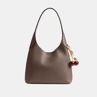 Sac à bandoulière en cuir marron avec une bandoulière courbée et un charm en forme de cerise doré fixé près du bord supérieur.