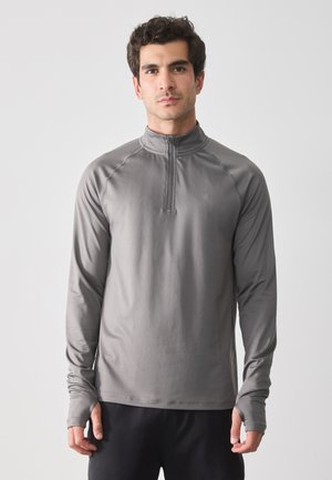 Gray long-sleeve pullover shirt with a quarter zip, smooth texture, athletic fit, and thumbholes at the cuffs, worn with dark pants.