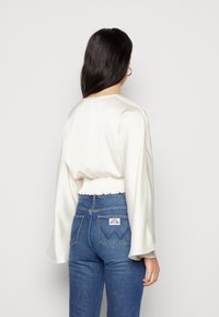 Vit satinblus med långa ärmar, cropped design och rynkad midja, som kompletteras av högmidjade blå denimjeans.