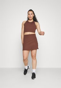 Smeđi crop top i odgovarajući mini suknja set napravljen od rastezljivog materijala. Odjeća ima prilagođeni dizajn i uparena je s crnim sportskim cipelama.