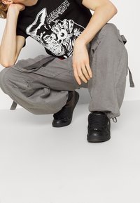 Camiseta gráfica negra con un estampado de temática de horror en blanco, combinada con pantalones cargo sueltos de color gris y zapatillas negras con detalles texturizados.