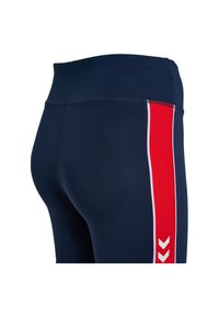 Donkerblauwe leggings met een hoge tailleband, voorzien van een rode zijstreep met witte accenten en chevronpatronen langs de buitennaad.