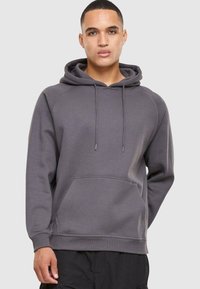 Sudadera gris con capucha tipo pullover, bolsillo canguro frontal, cordones en la capucha y puños acanalados, fabricada con una suave tela texturizada.