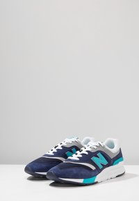 Sotilaslaivaston väriset mokkasneakersit, joissa on valkoisia yksityiskohtia ja turkooseja elementtejä. Varusteina pehmustettu pohja, nauhakiinnitys ja merkittävä 'N' logo sivulla.