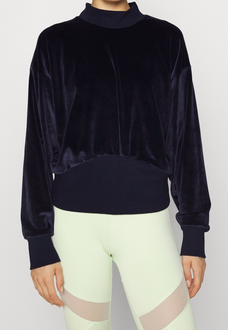 Sweatshirt en velours bleu marine avec un col montant, une coupe ample et des poignets côtelés. Caractérisé par une texture douce et un ourlet froncé. Associé à des leggings vert clair.