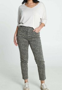 Pull ample de couleur beige clair avec un col en V. Jean olive vert à motifs avec un design paisley. Baskets blanches avec des accents scintillants.