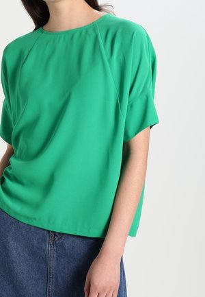 Groen kort mouwtopje, lichtgewicht stof, ronde halslijn, losse pasvorm, met raglanmouwen en subtiele plooien, gecombineerd met een denim rok.