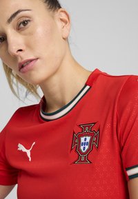 Rde športno majico iz zračnega materiala, ki ima belo Puma logo in v živih podrobnostih nacionalno znamko Portugalske.