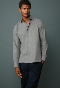 Gray long-sleeve button-up shirt with a small check pattern, featuring a pointed collar and black buttons, paired with dark pants.