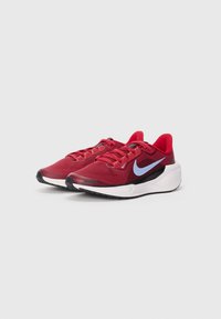 Baskets de sport rouges avec une tige en maille respirante, accents noirs, logo swoosh Nike bleu et une semelle blanche rembourrée.