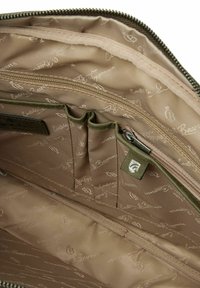 Beiger Innenraum einer Tasche mit dezenten Logo-Mustern, ausgestattet mit einem Reißverschlussfach und mehreren Taschen aus Stoff zur Organisation. Texturierte Futter.