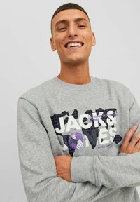 Sudadera gris con puños acanalados que presenta un gran diseño gráfico en negro, blanco y púrpura, que representa un mapa del mundo y texto.