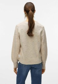 Maglione a maglia crema con bubbole texture, scollatura rotonda e bordo a coste. Indossato con jeans in denim blu, caratterizzati da una vestibilità rilassata e gamba dritta.