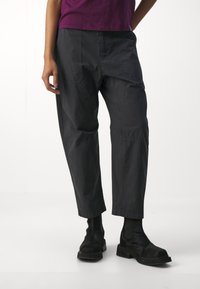 Pantalones ligeros de color gris oscuro con un corte relajado, que presentan bolsillos laterales y puños elásticos, combinados con botas negras hasta el tobillo.