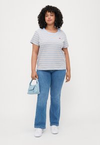 Camiseta a rayas en azul claro y blanco con cuello redondo, combinada con jeans de mezclilla azules. Sosteniendo un pequeño bolso azul claro.