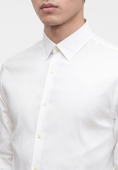 Close-up of a man wearing a plain white buttoned shirt with a classic collar, showing his lower face and upper torso.