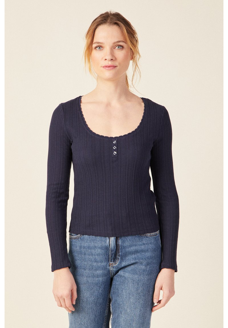 Top a maniche lunghe ribbed blu marino con scollo rotondo e orlo scallop, caratterizzato da tre bottoni frontali e un design aderente.