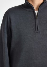 Pullover in maglia grigio scuro con colletto alto e chiusura a metà zip, caratterizzato da una texture liscia e una vestibilità comoda. Design minimalista, senza motivi.
