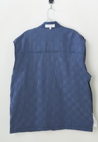 Cămașă fără mâneci de culoare bleumarin, cu un model texturat în carouri, având un guler și o margine dreaptă. Eticheta de pe spate afișează "sister jane."