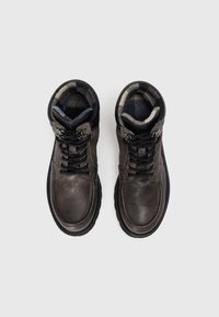 Bottines en cuir marron avec des lacets noirs, un col rembourré et une doublure à carreaux. Bout rond et semelle en caoutchouc robuste pour une bonne traction.
