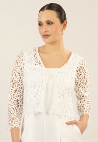 Weiße, kurze Jacke aus kunstvollem Blumen-Spitze mit hochgekrempelten, dreiviertellangen Ärmeln und einer Knopfschließe vorne. Glatte Innenauskleidung.